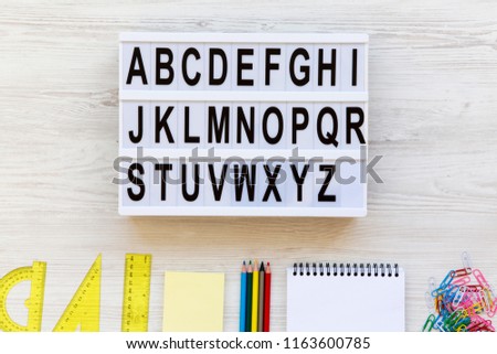 Education concept. Letters from A to Z. English alphabet on modern board and accessories for study over white wooden background, overhead view. From above, flat lay, top view.