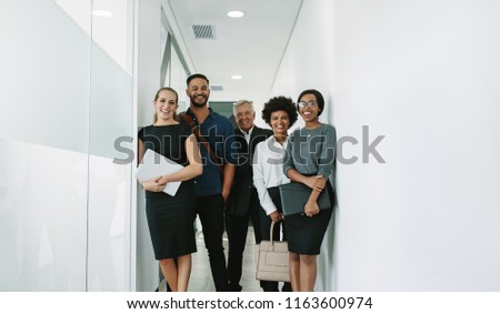 Portrait of happy business group standing together in office corridor. Multiracial business professional in office hallway.