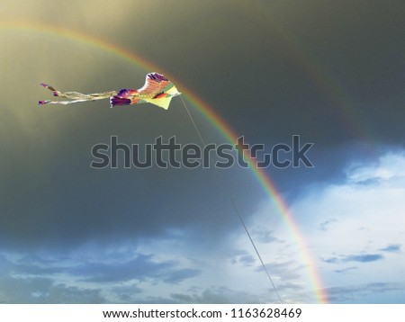Bright kite in the form of a bird in the sky with a rainbow and dark clouds after the rain in summer.
