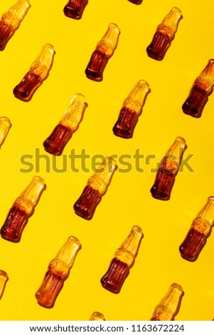Array of cola bottle shaped gummy candies against saturated yellow background.