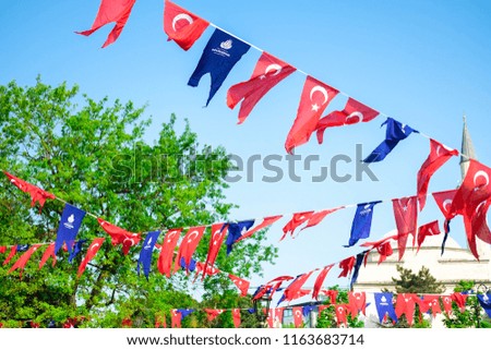 Many red flags of Turkey and blue flags of metropolitan municipalities decorate at Hippodrome square against of green leaves and blue sky. Turkish text means metropolitan municipalities.