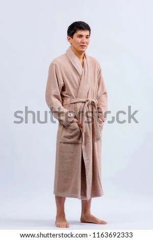 Asian guy in a bathrobe. A Kazakh man in a dressing gown on a light background. Royalty-Free Stock Photo #1163692333