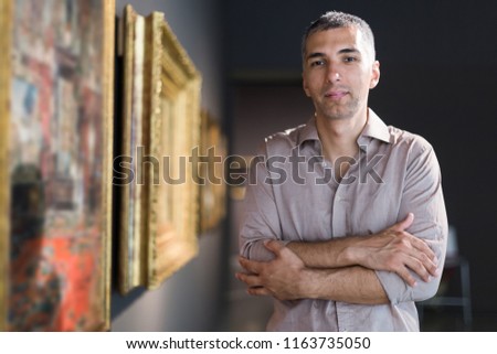 Adult man is visiting museum and looking at the pictures in the gallery indoor.
