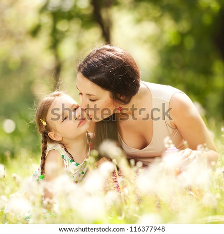 Happiness and harmony in family life. Happy family concept. Young mother kissing her daughter in the park. Happy family resting together on the green grass. Family having fun outdoor