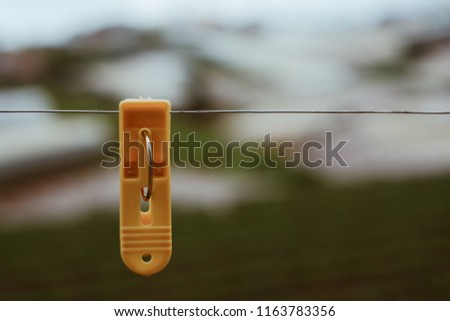 Alone plastic clothes peg. Royalty high quality stock photo of a yellow plastic clothes peg clothespin clipped on outdoor clothesline metal line. Green garden background