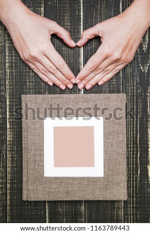 White woman making heart gesture with hands near family photo album isolated on wooden brown background. Overhead vertical shot. 