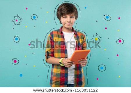 Modern tablet. Calm teenage boy looking glad and smiling while standing with his modern tablet after getting it for his birthday
