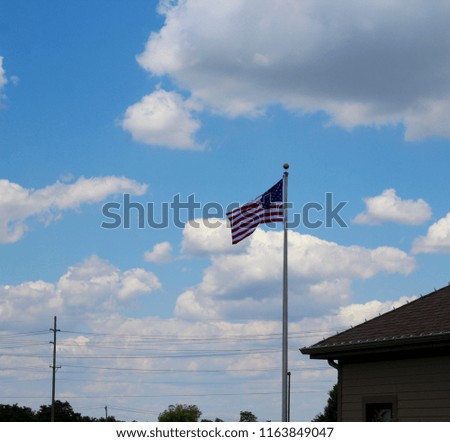 The flag waving in the breeze of the wind with the white clouds in the blue sky.