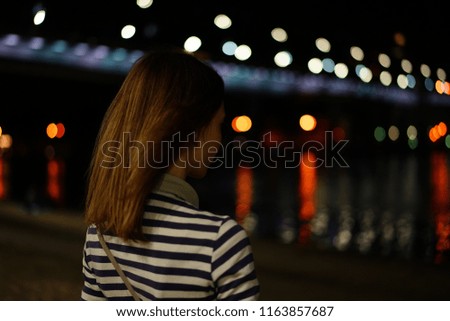 Girl with hair developing in the wind stands on the Bank of the river against the background of the lights of a big city, looking into the distance, thinking about the future. Escape from civilization