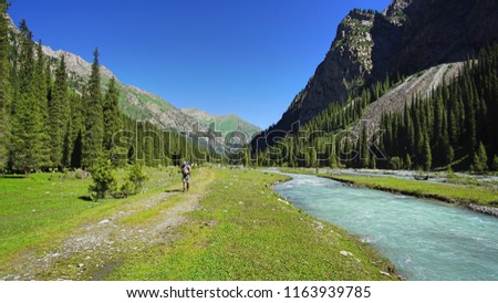 one man hiking in the mountain between a lush green forest and a blue river.  