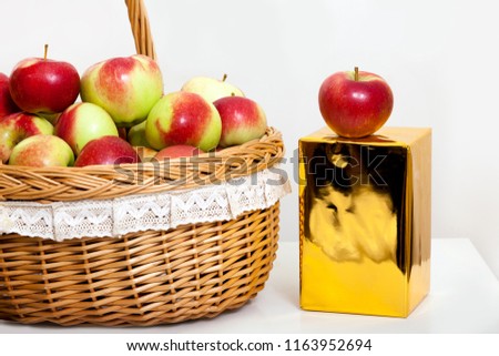 Red and yellow apples in a basket on white background. Close-up of juicy fruit with gold gift box.