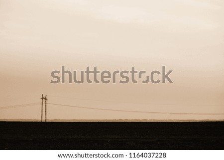 Power lines on background of sky close-up. Silhouette of electric pole with copy space in sepia tones. Wires of high voltage above ground. Electricity industry in monochrome.
