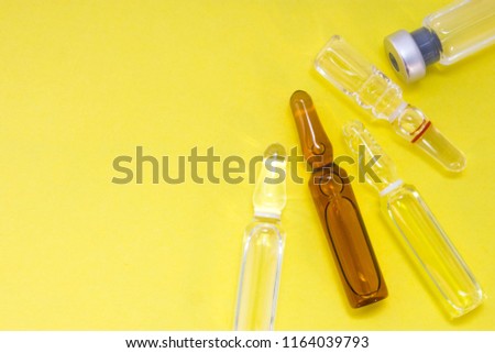 Glass vials with medications and drugs are on yellow uniform background view from above with clear area of half photo for labels, headers. Concept photo for pharmacy, treatment, scientific research