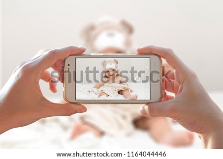 Woman photographing her baby with a cell phone. Photo camera of a smartphone. 
