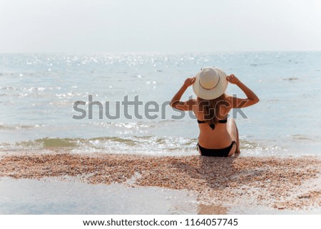 Young girl in a yellow hat and bikini on the beach in the summer season