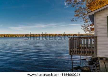 Cottage Country Fall Scene featuring cottage balcony overlooking blue lake and beautiful shoreline with trees in fall colors