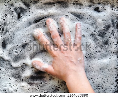 Car washing service. A woman's hand in foam is washing the dirty surface. Wash the greasy baking sheet.