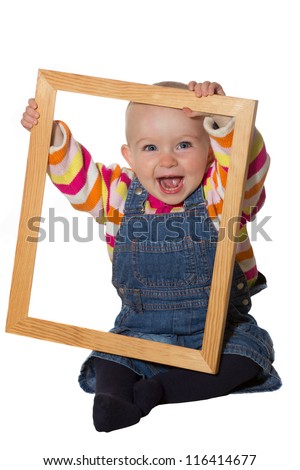 Laughing vivacious little baby girl playing with an empty wooden picture frame looking through it at the camera