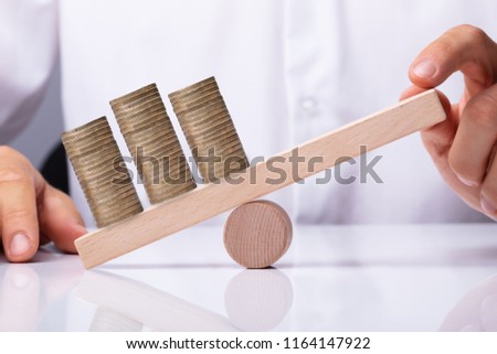 Human Hand Balancing Golden Stacked Coins On Wooden Seesaw Royalty-Free Stock Photo #1164147922