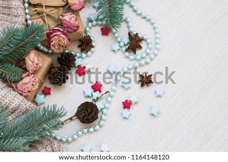 Christmas composition. Gifts, wool blanket, cones, badon, paper stars, a Christmas tree, beads and roses on a light wood background