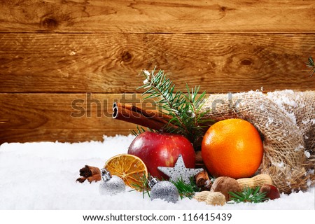 Artistic still life with festive spices and fresh colourful fruit lying in a hessian bag on fresh snow against a wooden backdrop with copyspace for your seasonal Christmas greeting