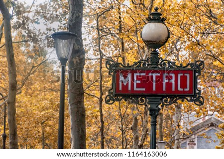 A city sign with a lamp signifying the entrance to the Metro Parisien, against the backdrop of yellowing autumn leaves. Paris. France