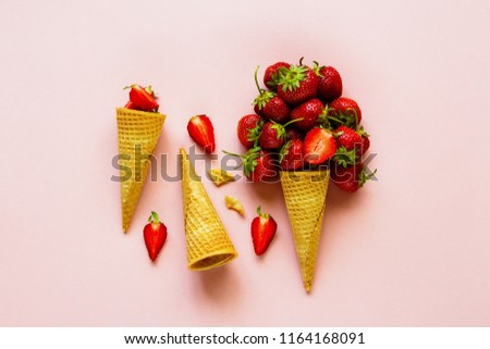 Spring or summer composition on pastel light pink background flat lay. Waffle sweet cone with fresh strawberry from above. Holiday mood concept. 