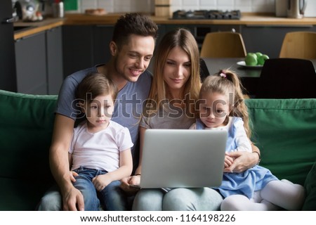 Young family with kids using laptop together sitting on sofa at home, smiling parents spending time with children son daughter relaxing holding computer shopping online or watching video in internet