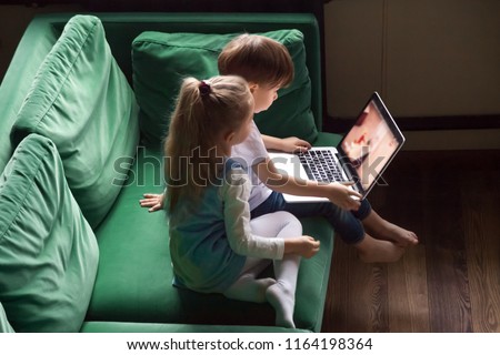 Siblings boy and girl enjoying kid cartoons on  using laptop together sitting on sofa at home, preschool children sister and brother focused on watching interesting video online spending time 