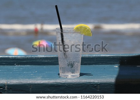 Cold refreshing drink with lemon slice  and straw on wooden bar at beach.