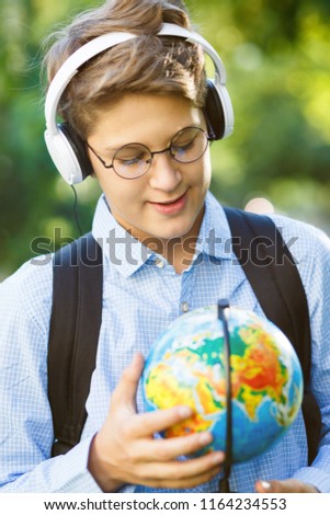 cute 11 years old boy in round glasses blue shirt, headpones holds a globe in his hands. Education, back to school concept