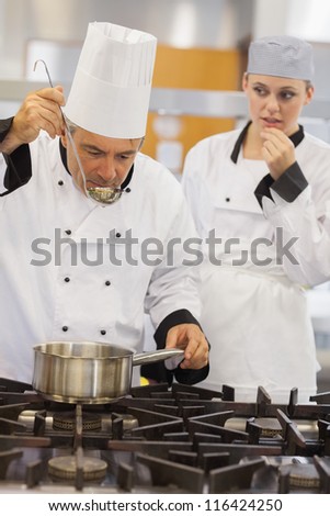 Teacher tasting his students soup with her watching anxiously in kitchen of culinary school