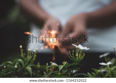 White flowers with background of a burning sparkler held with two hands