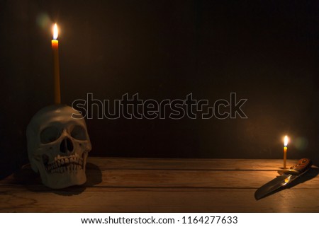 Human skull with candle light and knife on wooden table in the dark background, Decorate for Halloween Theme with copy space.