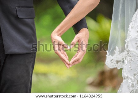 Bride and groom making a hand as heart shape together in the park as a sign of love and care.