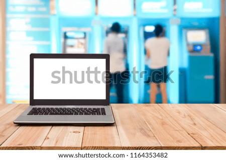 Computer on the table, blur image of people stand at ATM machine as background.