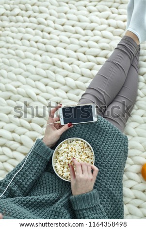 Very cozy picture for the autumn, September, October, November. A girl is watching movie on phone with headphones and eating popcorn. Green screen on your mobile for your picture, text, information.