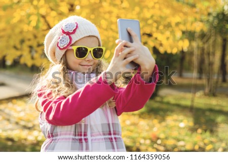 Pretty girl of 7 years doing selfie using smartphone, autumn background