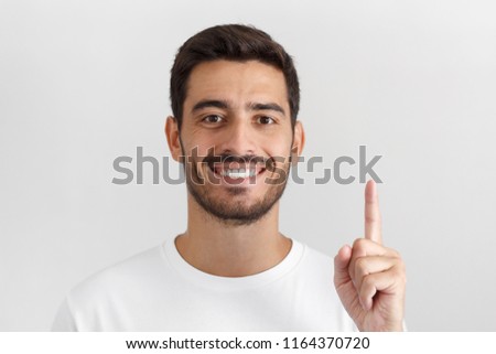 Handsome smiling young man in white t-shirt pointing up with his finger, isolated on gray background