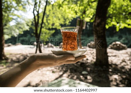 Eastern black tea in glass on woman`s hand at forest. Eastern tea concept. Armudu traditional cup. Green nature background. Selective focus