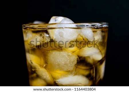 a glass of blur yellow alcohol beverage with full ice cubes in black background