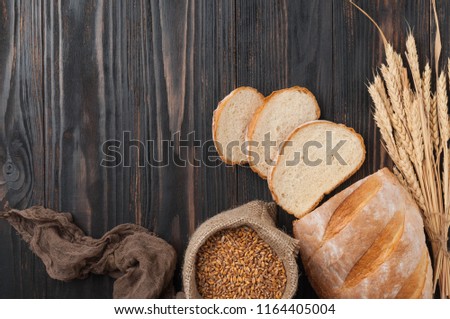 Bread. Loaf of white wheat bread, sliced on a brown wooden table with a bag of wheat grains and wheat spikelets. Top view. Copy space. Rustic.