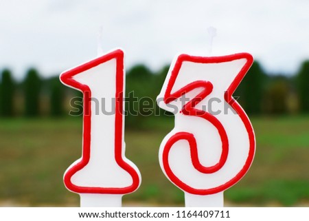 Colorful birthday candle in shape of number 13 ready for burning outdoors on green landscape background with copy space for text on sky and grass. Happy birthday party invitation and greeting card con