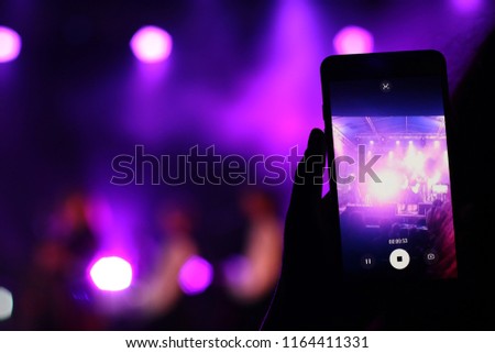 Shooting festival concert on smartphone with place for text. Blurred music stage bokeh background for design. Fans takes picture of scene on phone