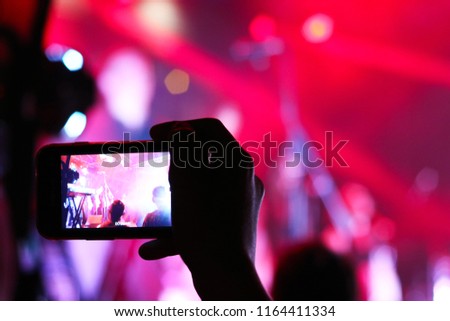 Smartphone shooting festival concert. Blurred music stage bokeh background for design. Fans takes picture of scene on phone