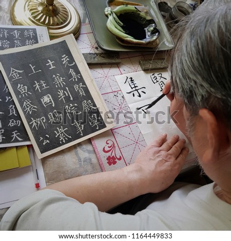 Grandpa is practicing Chinese calligraphy with black ink (translation of the characters: Yin, Yang, union, gold, study, peace, life)