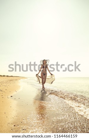 slim young woman in swimwear with pareo walking on sea shore toned image