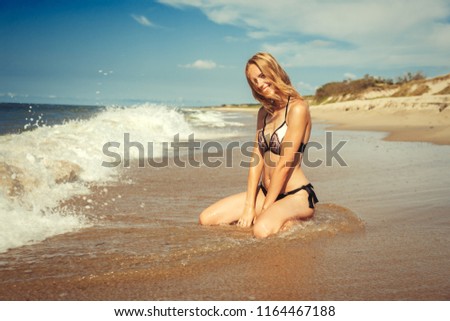 young blond woman in swimsuit at sea surf with foam sitting