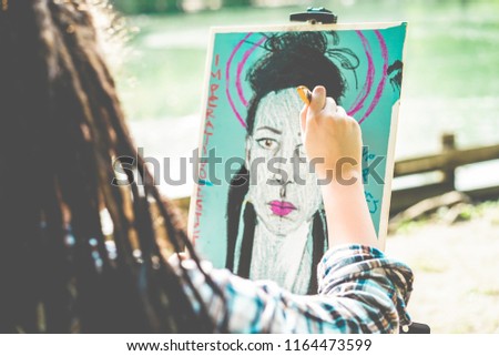 Artist girl painting self-portrait in city park outdoor - Young painter woman with dreadlocks at work - Contemporary art, millennial generation and youth lifestyle concept - Focus on her hand