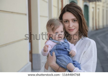 Young mother with her baby girl on the street, candid portrait image, natural lighting, family life concept